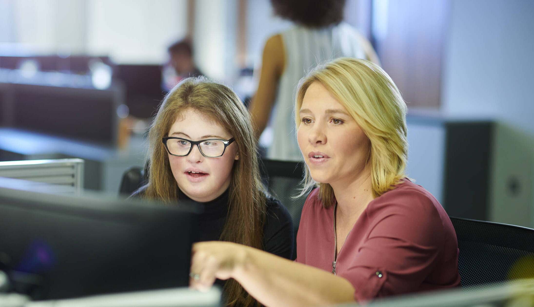Two young female coworkers talking at a computer screen