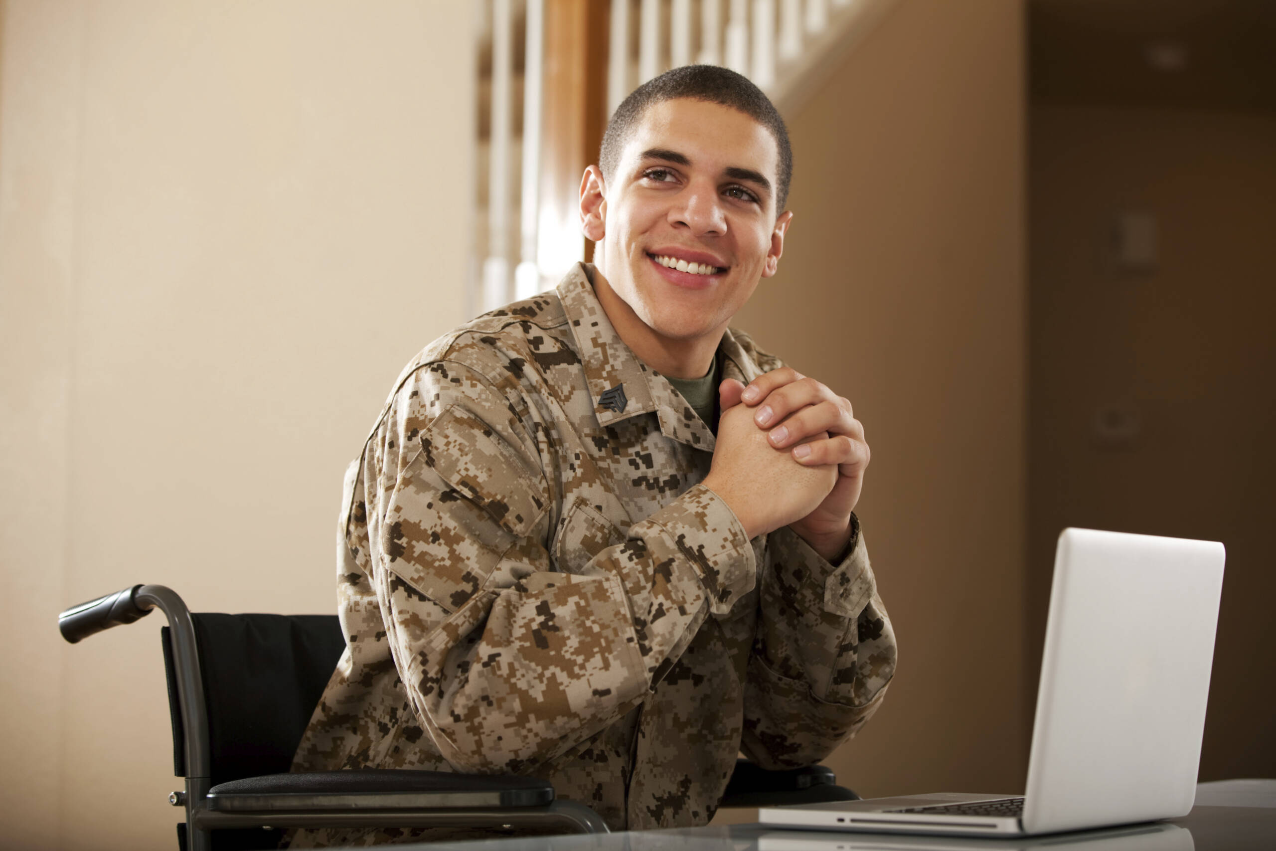 Man dressed in military uniform. He is sitting in a wheelchair with a laptop.